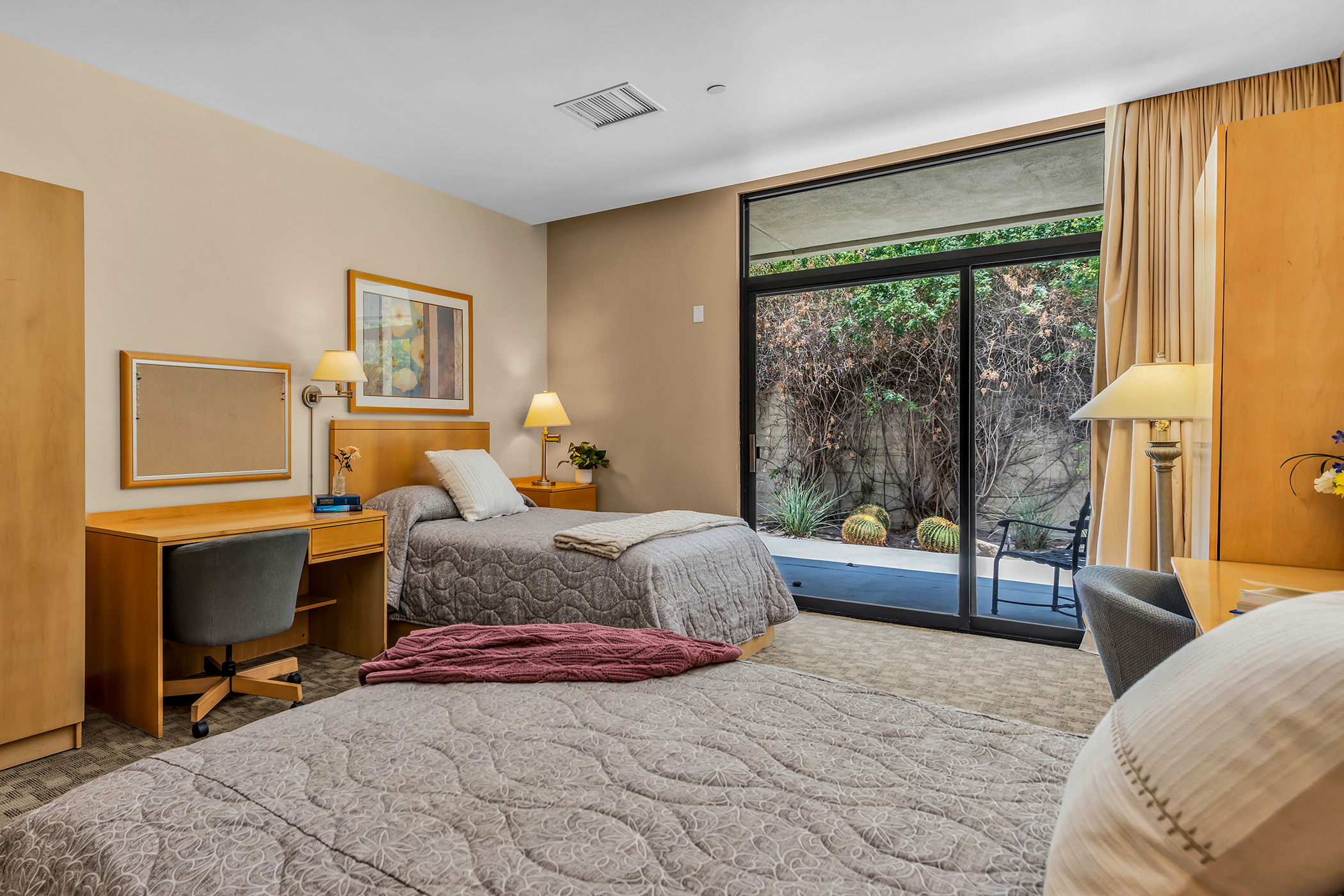 Inside a shared room with two comfortable beds, dressers, and a patio with desert plants